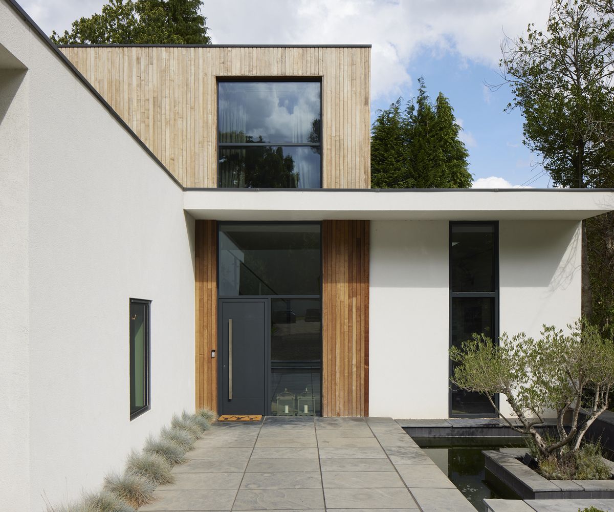 A paved pathway up to a modern home and front door with white masonry and timber cladding