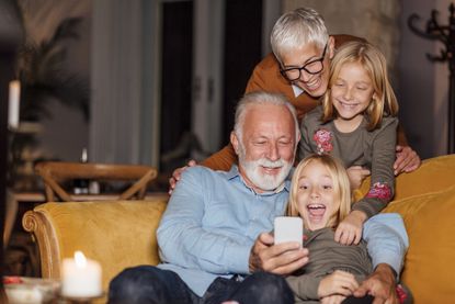 Grandparents with their two granddaughters looking at pictures on a smartphone, spending some quality time together, having fun.