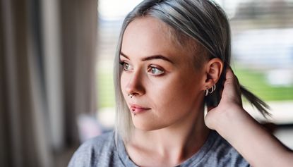 Front view portrait of young woman with multiple ear piercings at home