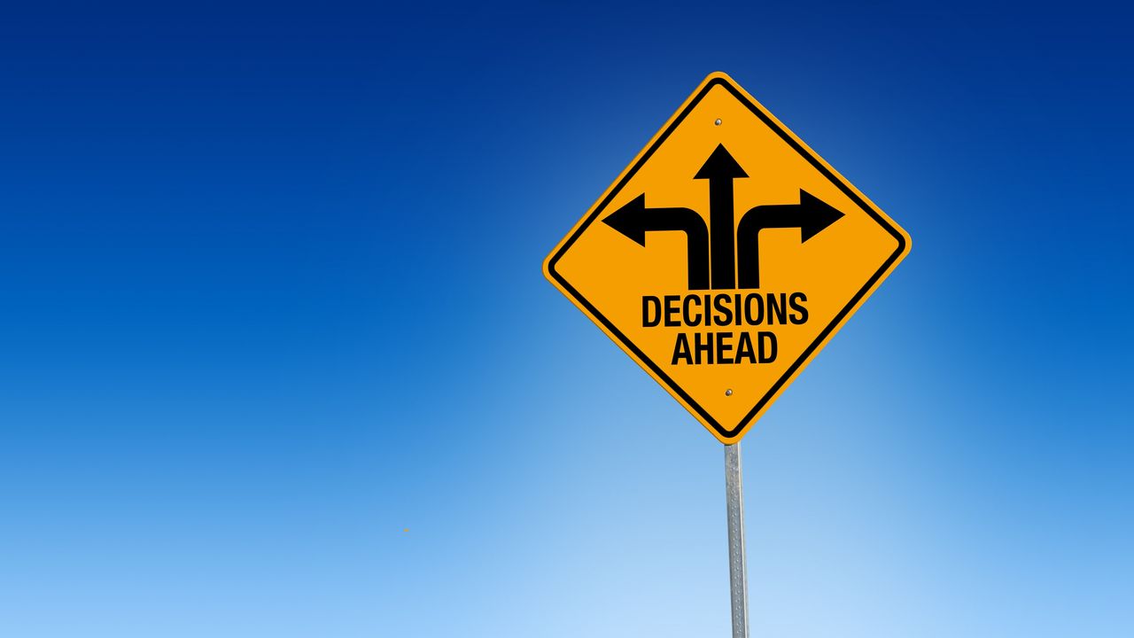 A yellow traffic sign has three arrows pointing in different directions and says &quot;Decisions ahead.&quot; 