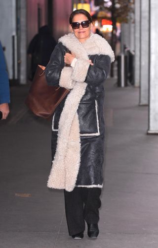 Katie Holmes walks to her broadway show wearing a shearling coat with black pants and a raisin brown tote bag