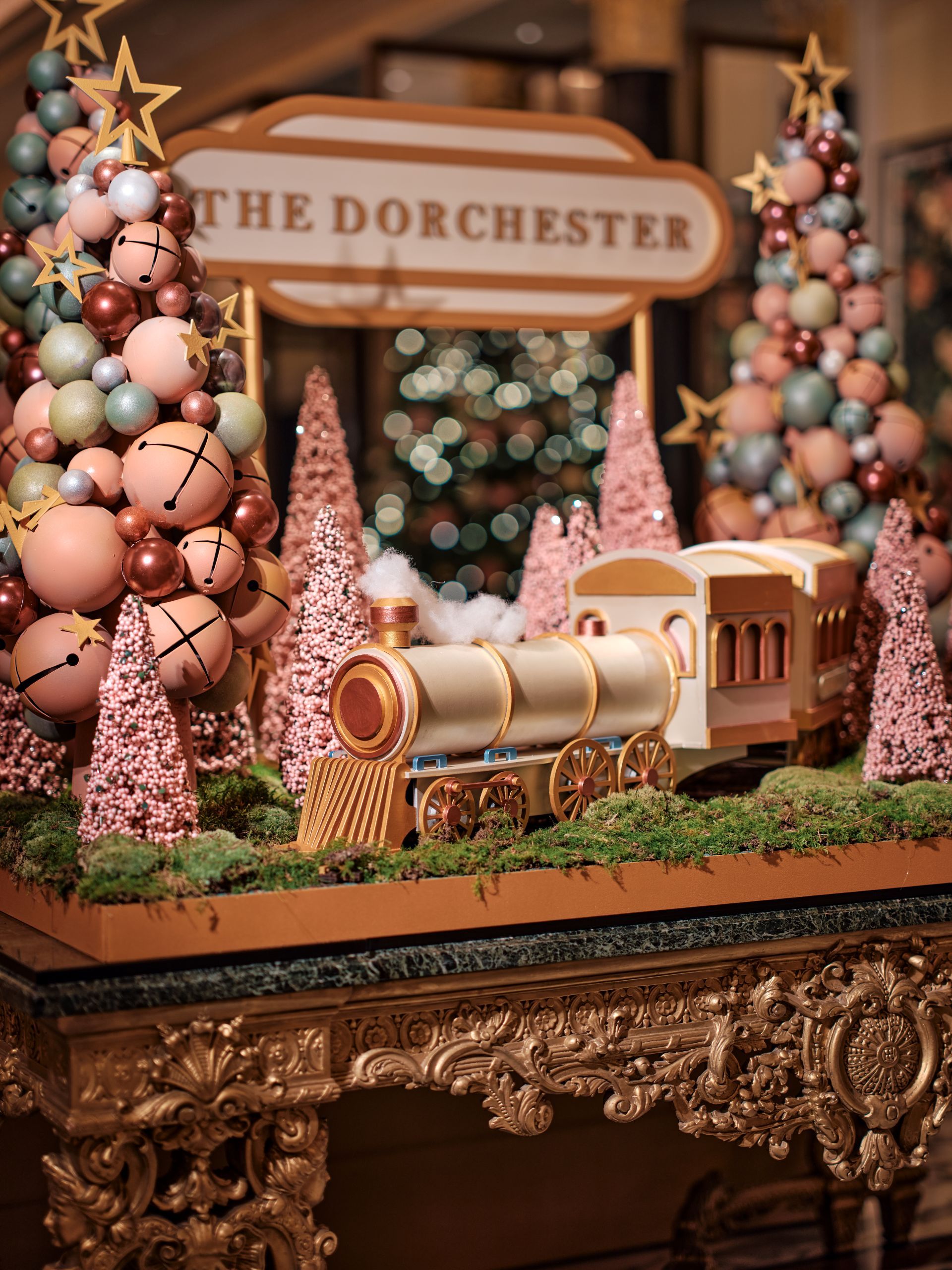 The Dorchester hotel decorated at Christmas with a central display of colorful bobble trees, pink smaller trees and an edible train in the middle of it on pretend, possible edible, grass