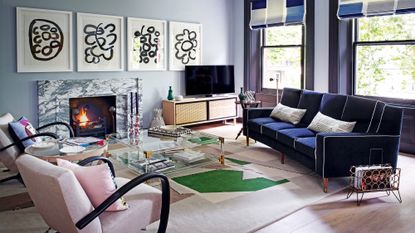 A blue living room with pale blue walls, a marble fireplace, dark blue sofa and pale pink armchairs.