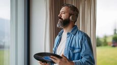 Handsome man listening to vinyl with headphones, standing by window