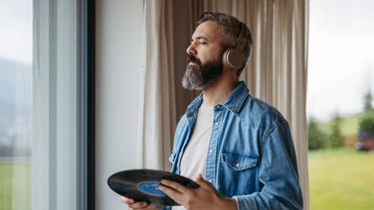 Handsome man listening to vinyl with headphones, standing by window
