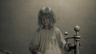 Emily, a blind girl with white hair and an old-fashioned white sleeping robe, sits on a bed in Resident Evil Requiem's care center