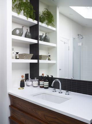 White bathroom countertop with inset basin, mirror above and shelving to one side