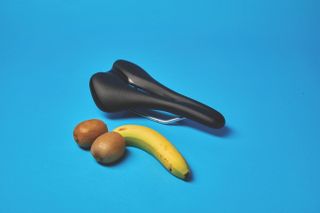 Two kiwi fruits and a banana next to a saddle on a blue background