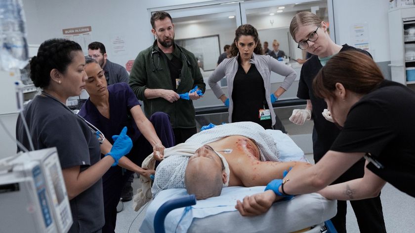 From left to right: Kristin Villanueva, Alexandra Metz, Noah Wyle, Sepideh Moafi, Taylor Dearden, Fiona Dourif all looking at a patient who is laying on a hospital bed. 