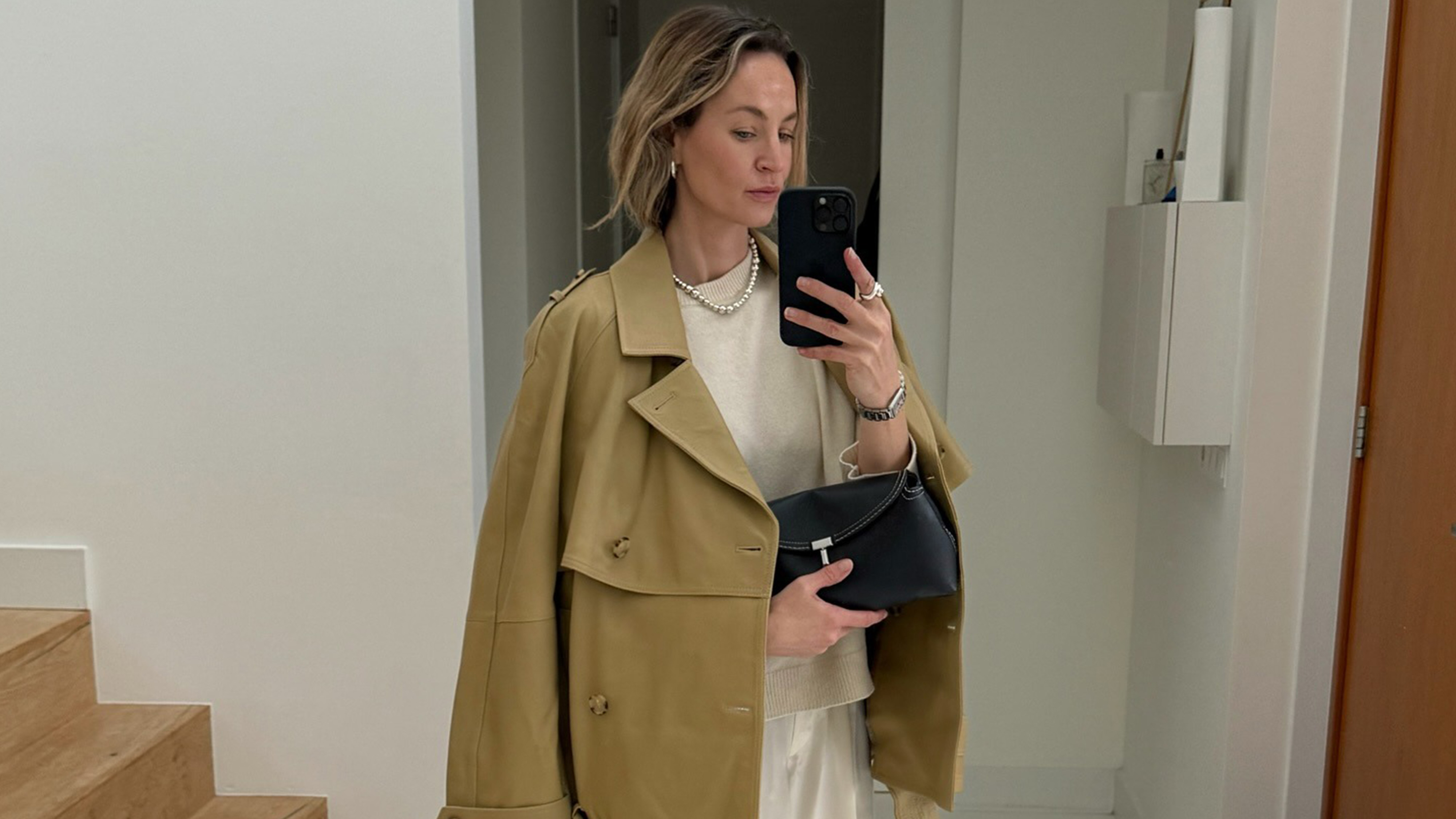 Anouk wears a trench coat, sweater, silk pants, and toteme clutch.
