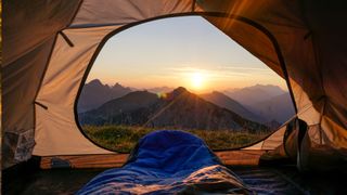 The doorway of a tent open with a view of trees and the sun