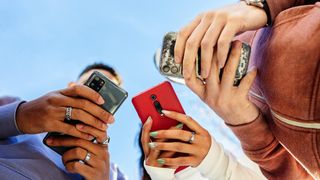 A colorful picture from below of three people using their smartphones.