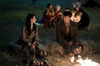 a woman and a soldier sit outside of a fire in a still from the k-drama crash landing on you