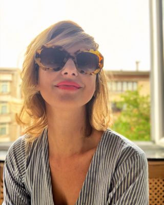 Kim De Craene wearing tortoise shell sunglasses and a striped blouse.