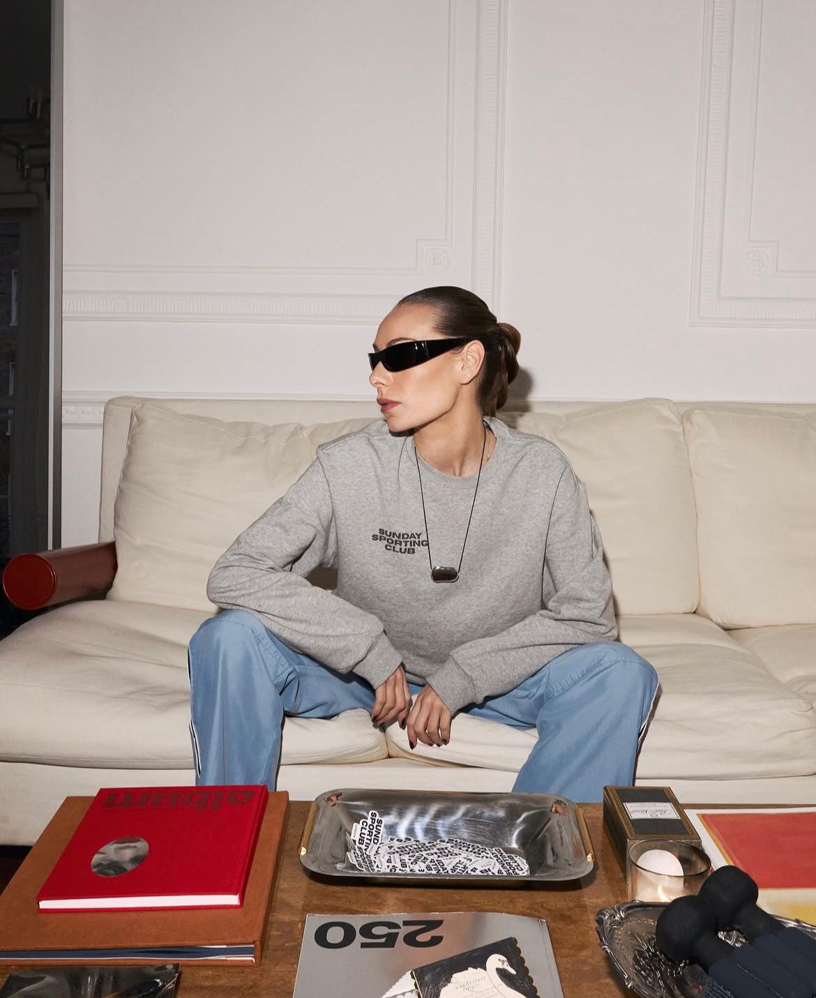 A woman wearing sunglasses looks to the right whilst sitting on a cream sofa