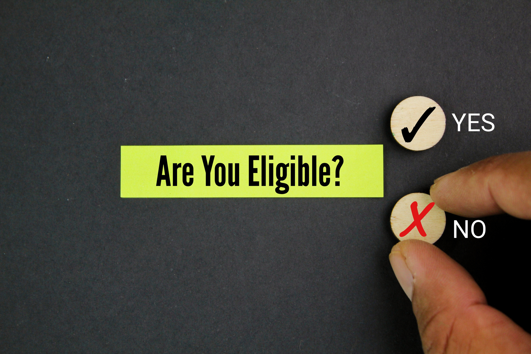 magnifying glass and hand holding colored paper with question word Are you eligible?