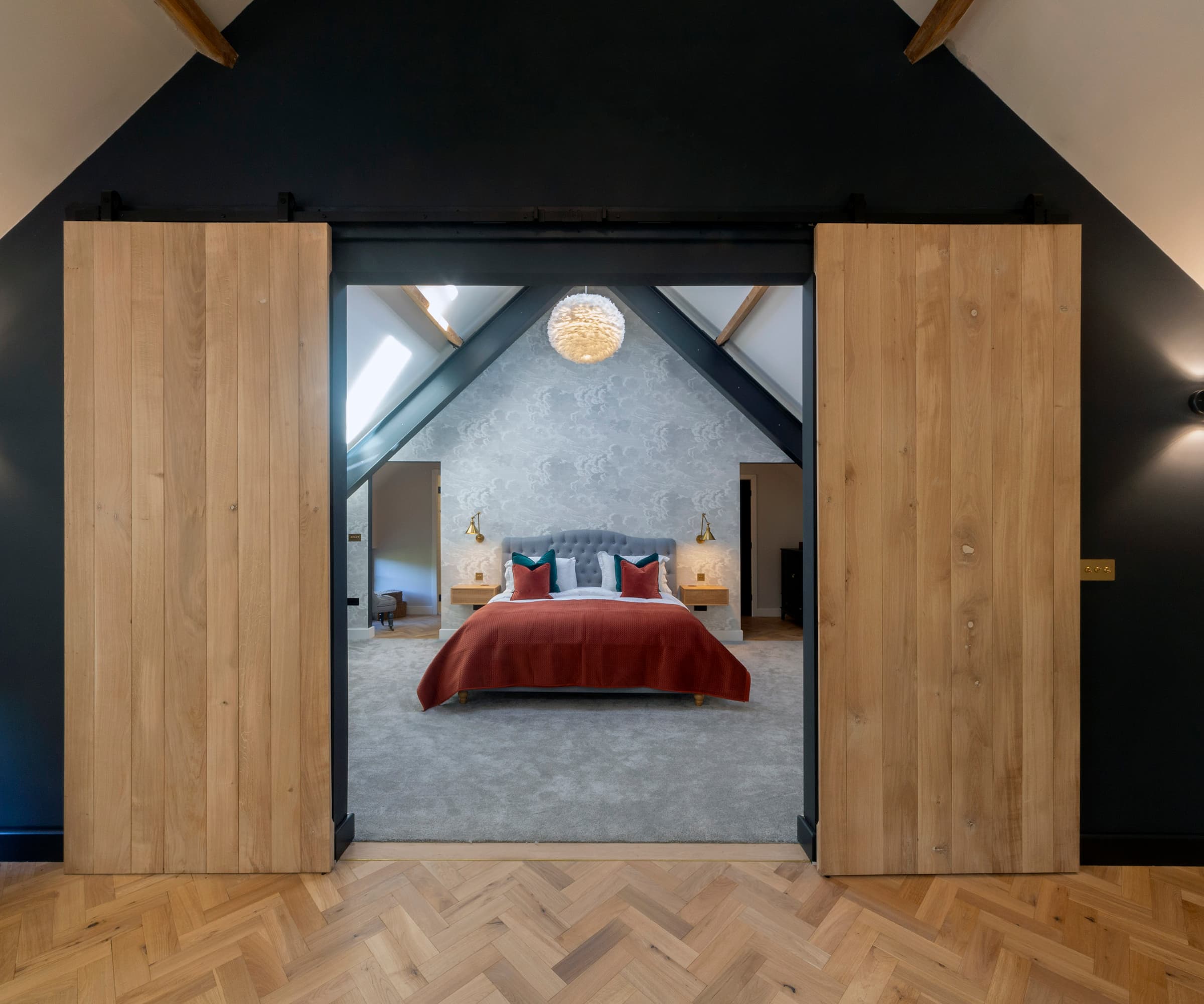 An upstairs bedroom with a triangle shaped roof and sliding wooden doors and wooden flooring