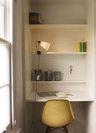 Home office built into a small alcove, with white desk and walls and a yellow chair