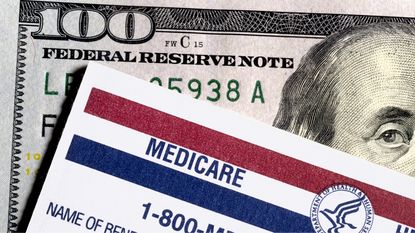 The top corner of a Medicare card sitting on top of a hundred-dollar bill.