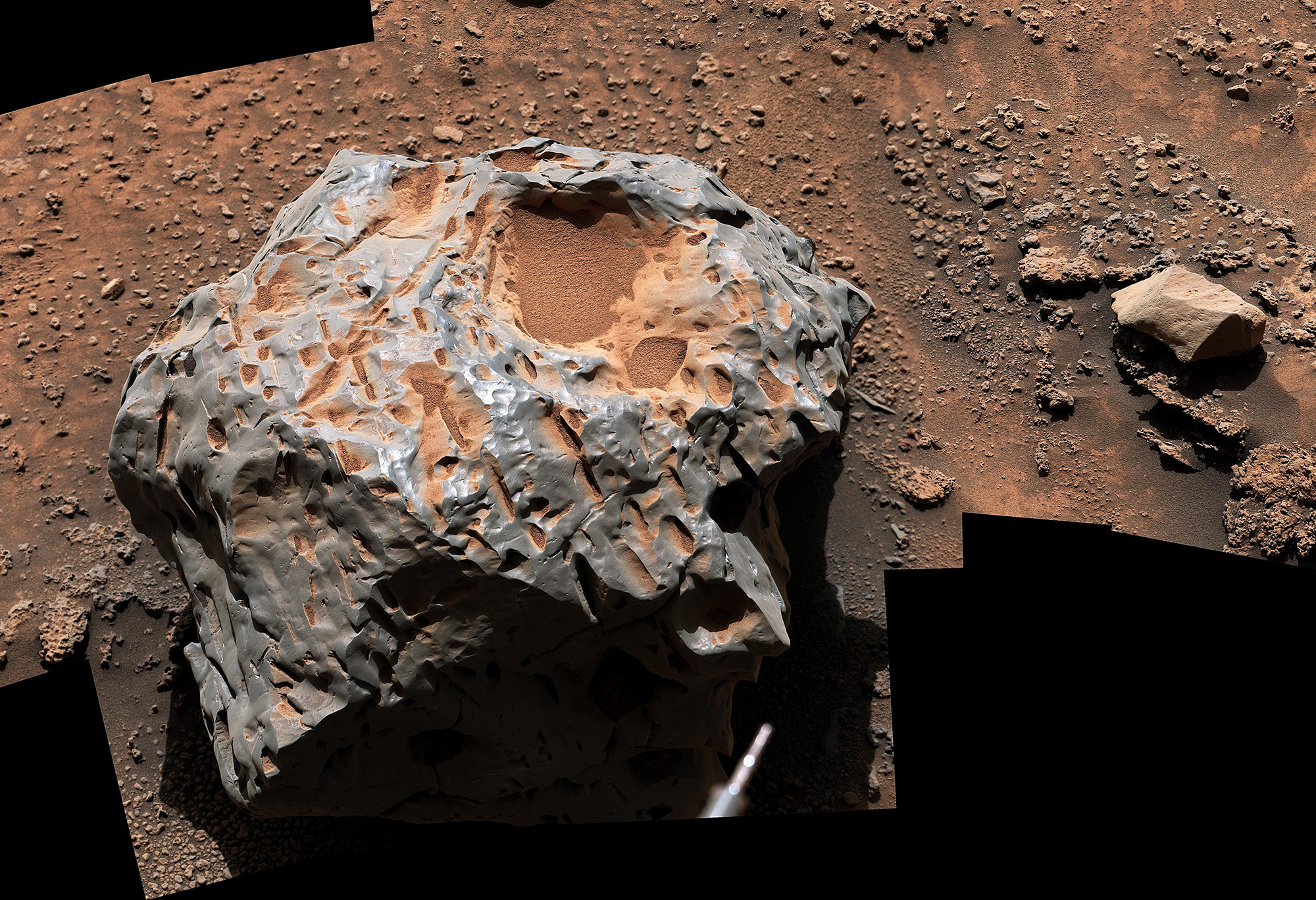 A close up of a large gray and red rock on a reddish surface.