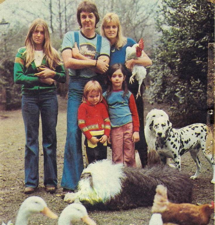 Paul McCartney and his family stands outdoors with several animals, including a dalmatian, chickens and geese, posed in a garden or yard.