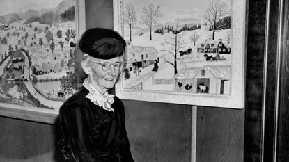 Grandma Moses stands in front of two of her paintings