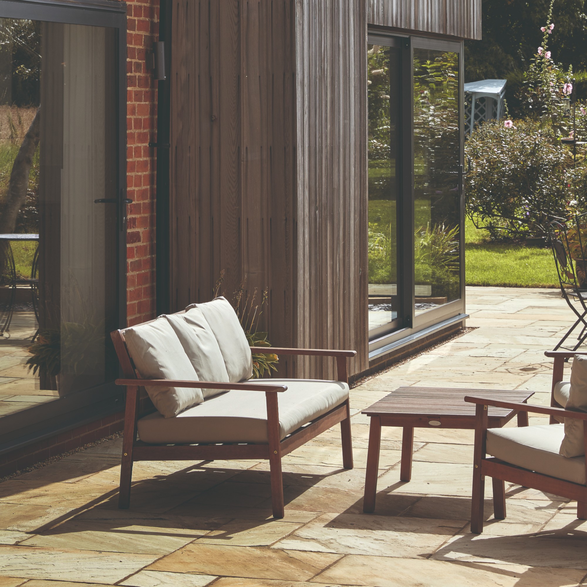 A patio with a wooden garden lounge set with cream seat and back cushions