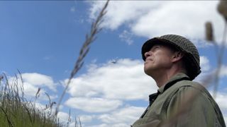 Person in army fatigues and helmet looking up at a blue sky