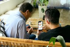 A senior man and his son order food on their phone while sitting on a couch.