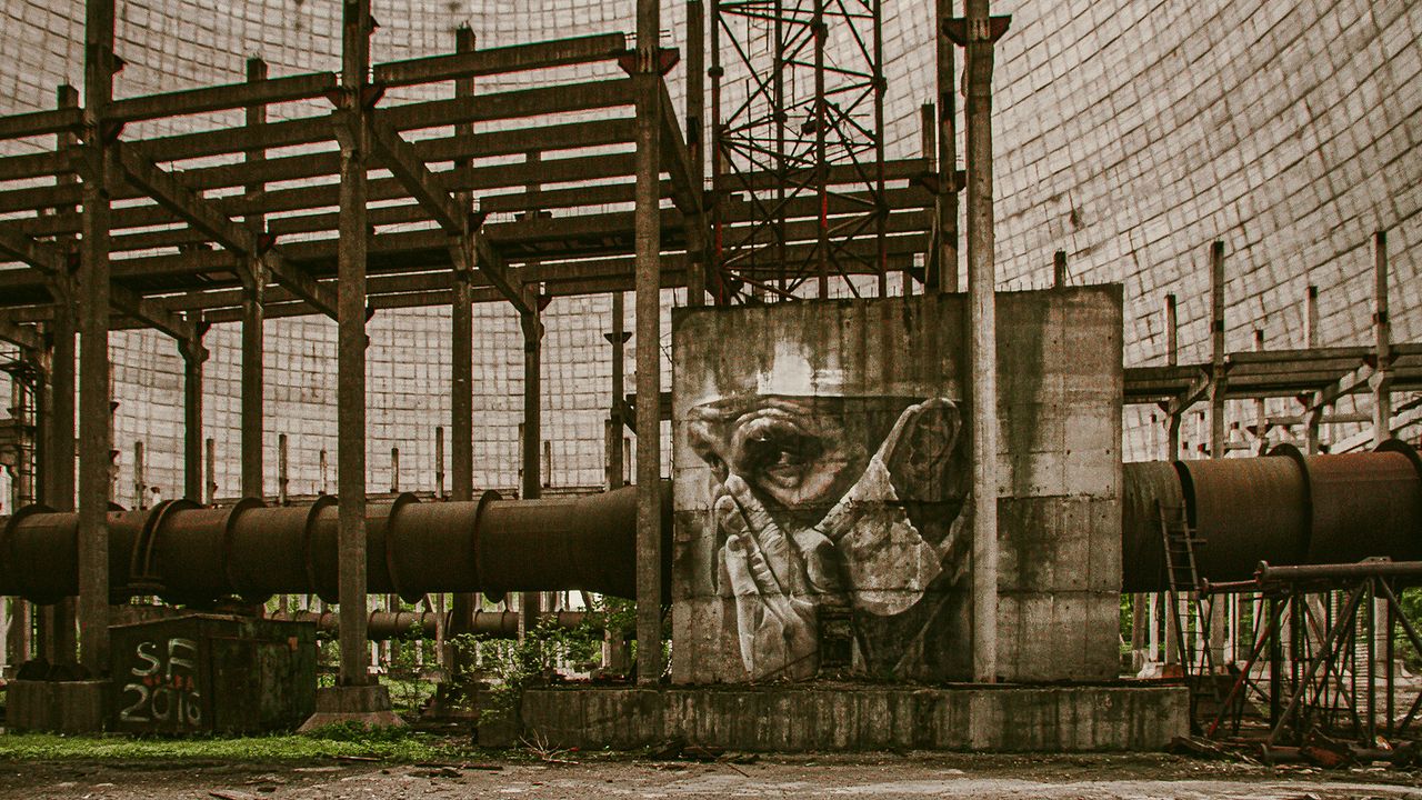 A view of a nuclear power plant with a mural of a person wearing a gas mask painted on a tower.