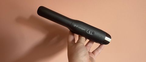 The GHD Unplugged being held against a coral background