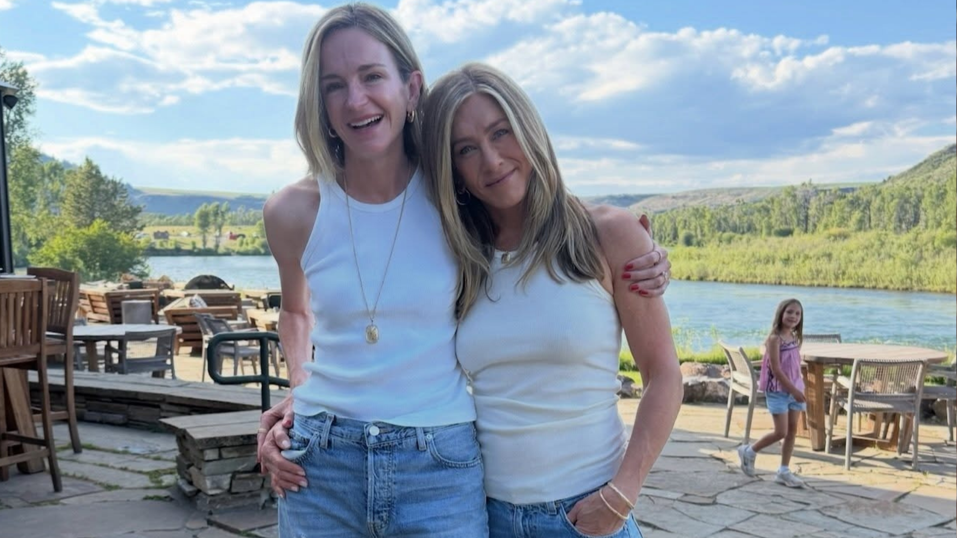Jennifer Aniston poses with Molly Kimmel lakeside, both wearing white tank tops and jeans. 