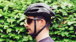 A man in a bike helmet and sunglasses in front of a hedge