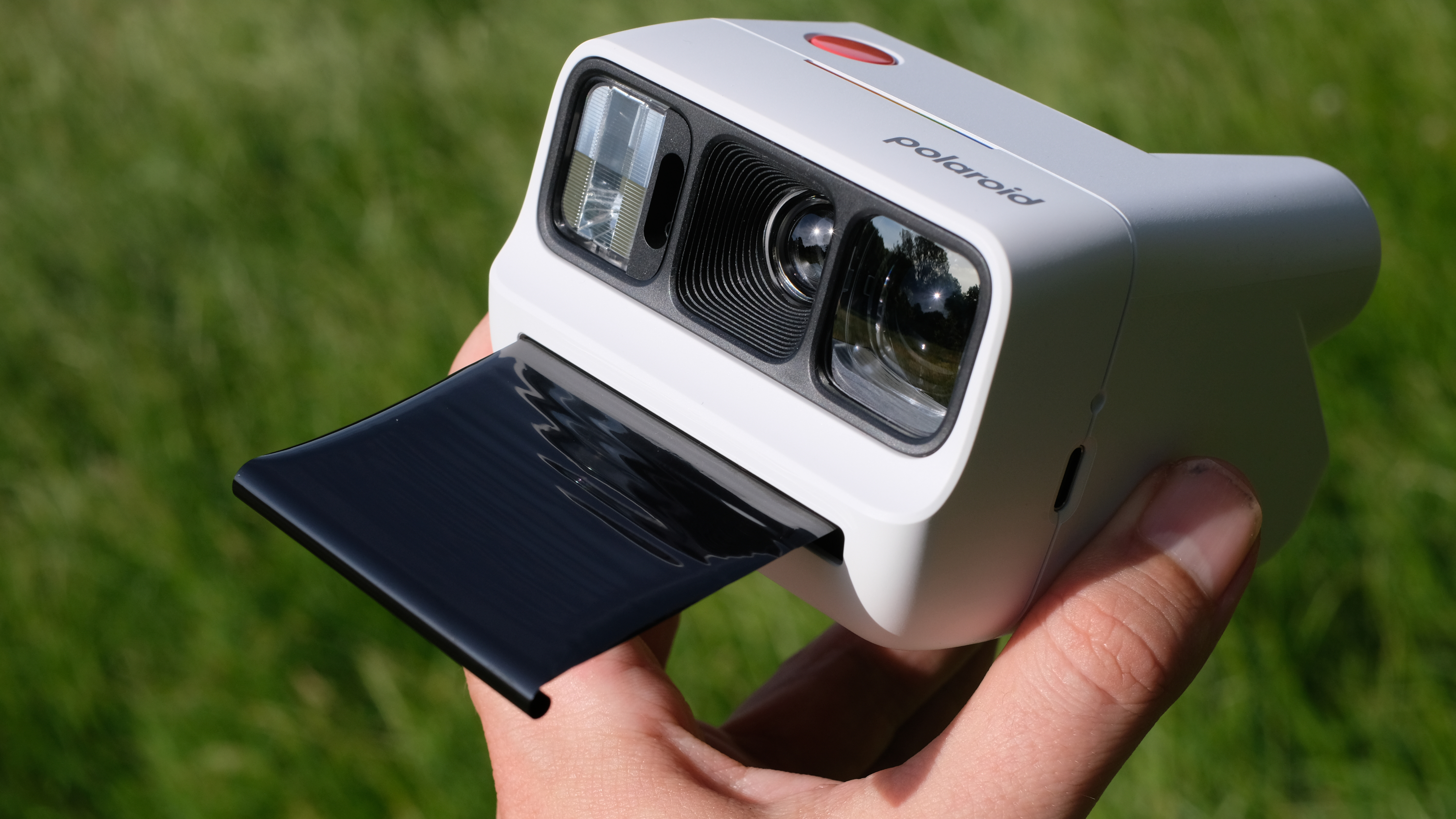 Photograph of man's hand holding Polaroid Go Gen 3 camera in white with film shield extended