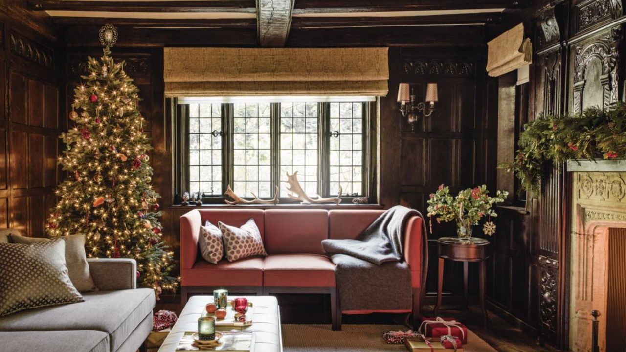 A cosy living room with two sofas, with exposed ceiling beams, a tall decorated Christmas tree and fireplace with a lit fire.