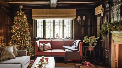A cosy living room with two sofas, with exposed ceiling beams, a tall decorated Christmas tree and fireplace with a lit fire.