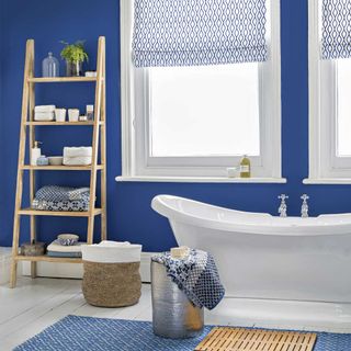 Ocean-blue bathroom with ladder storage unit and patterned blinds