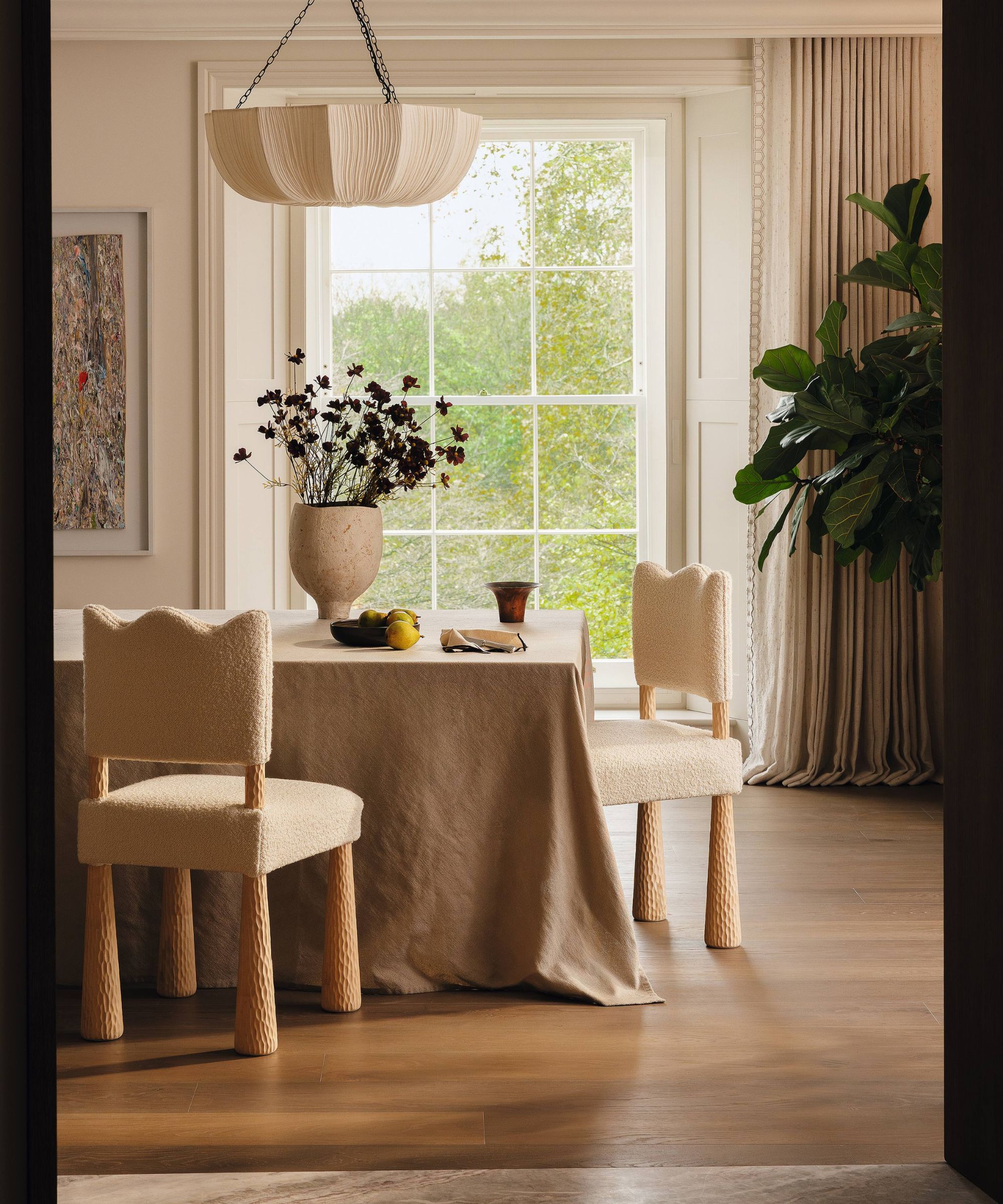 a light neutral dining room with a large window, wooden floor, a table with a linen cloth and curved dining chairs
