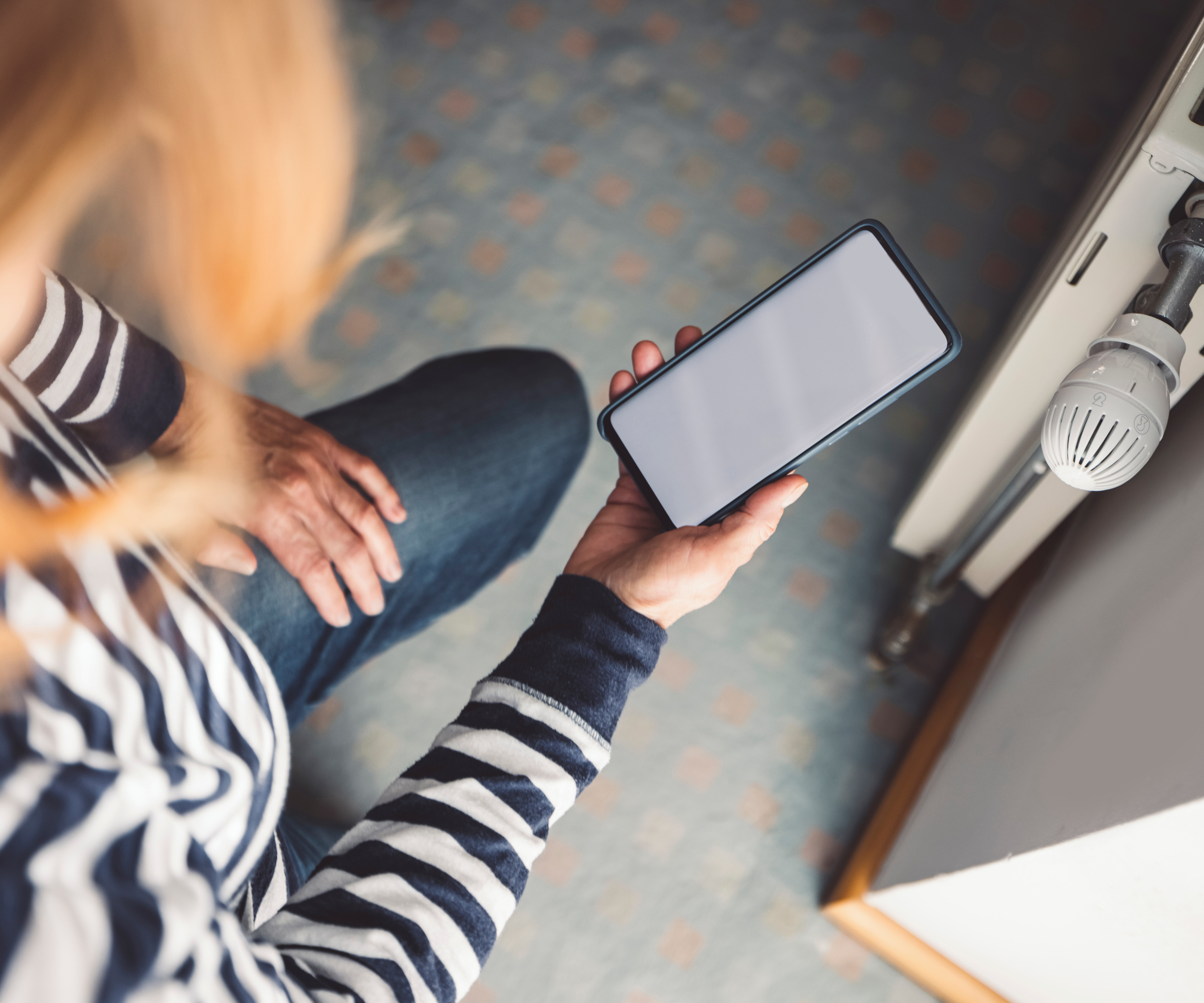 woman looking at phone screen stood next to radiator