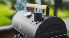 Smoke coming out of a smokestack of a small black smoker grill or barbecue on green background