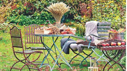 Metal bistro set on lawn in autumn garden with brown leaves and harvests including apples