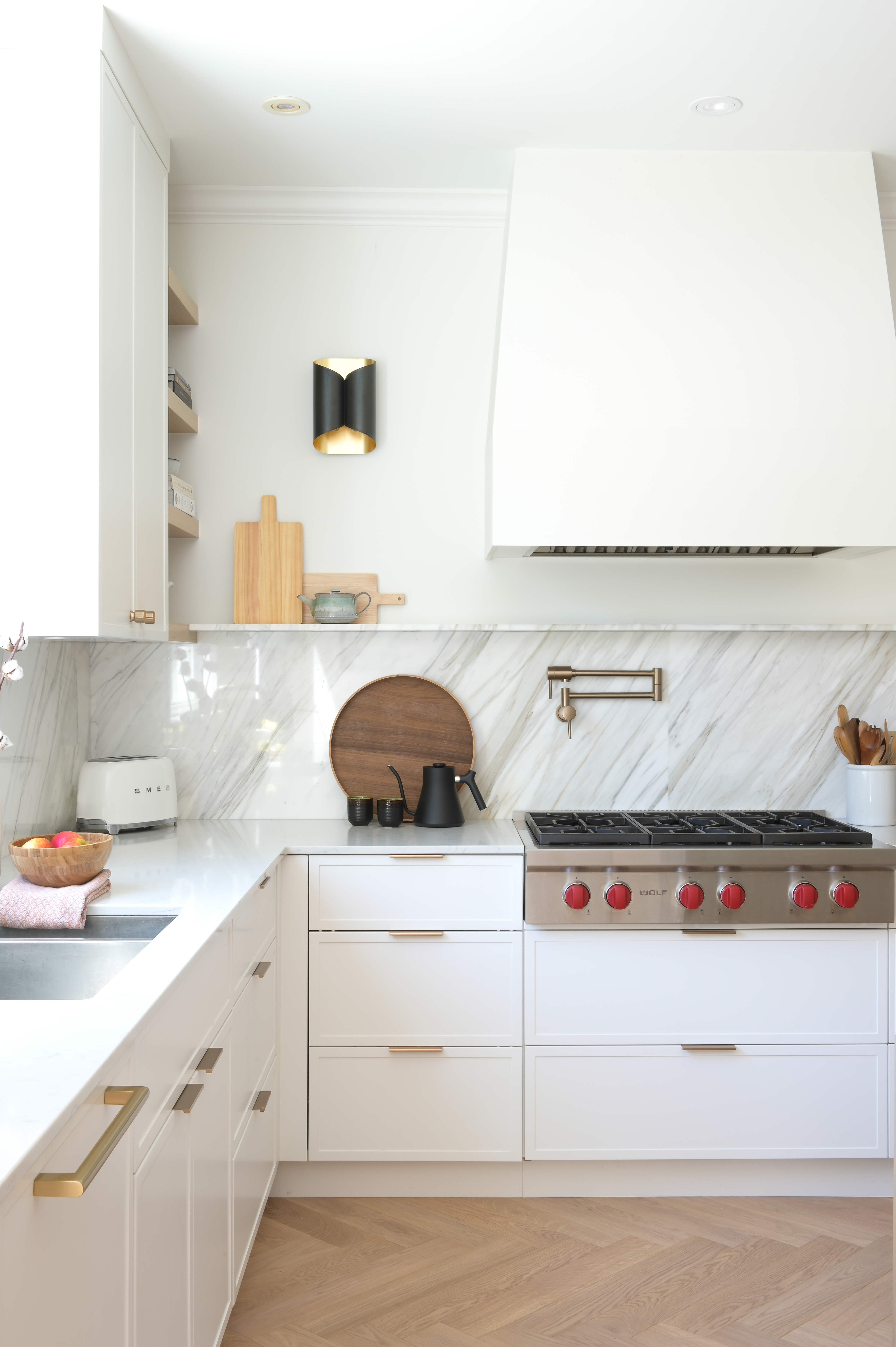 An all-white kitchen with wooden flooring, with brass hardware