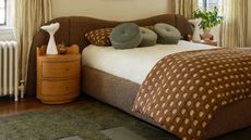 Cream bedroom with bed with large brown beadboard and wooden circular side tables and green rug