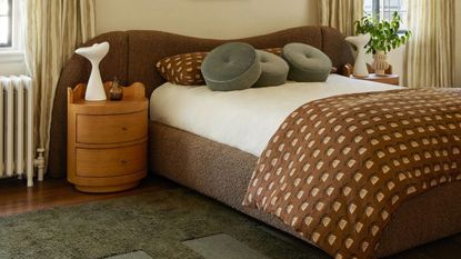Cream bedroom with bed with large brown beadboard and wooden circular side tables and green rug