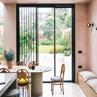 dining room table and chairs in a room with pink walls, and sliding doors into the garden