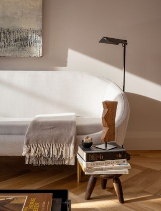 A sofa with a blanket on top with a side table and books next to it