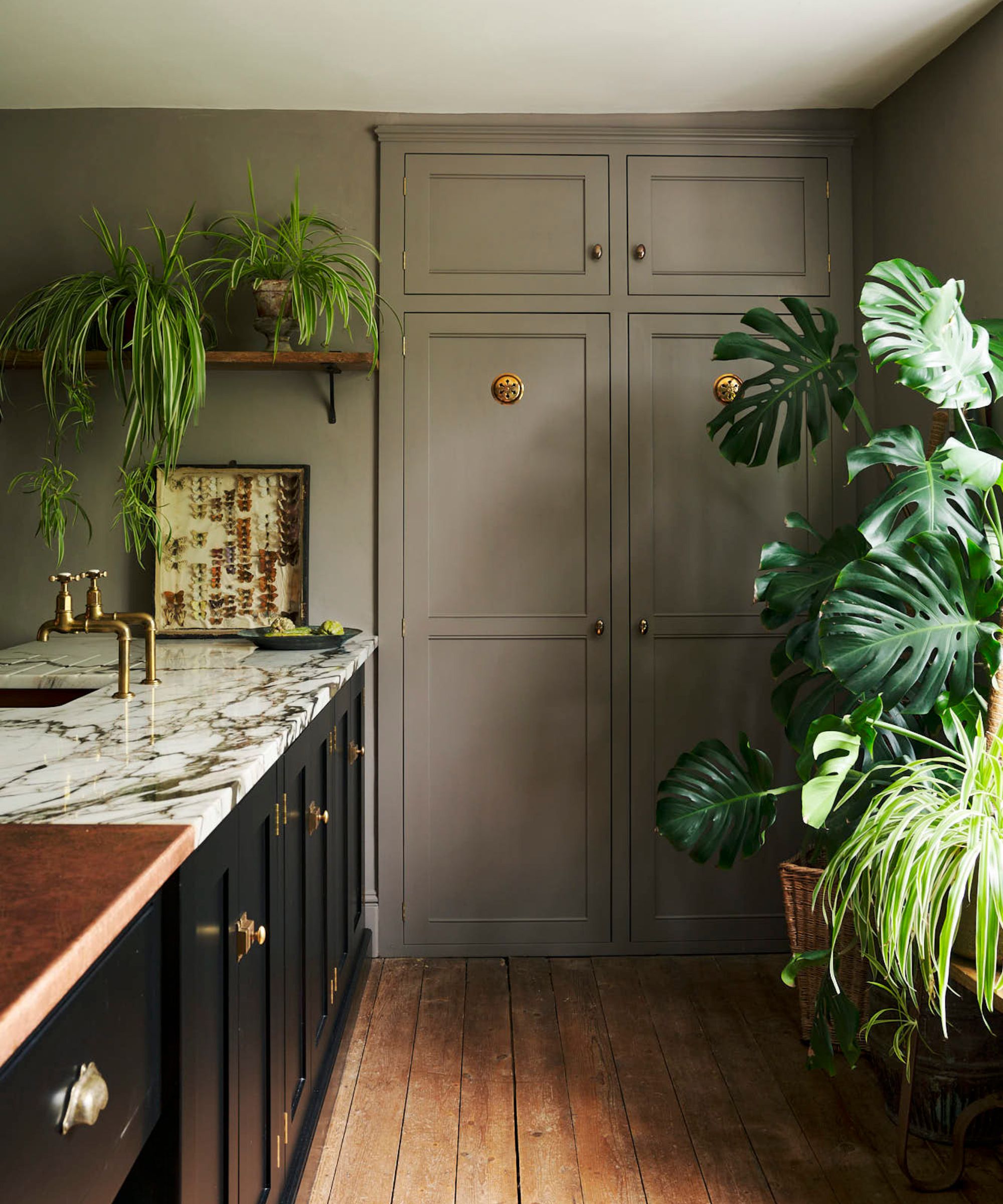 A light green kitchen with a black island and brass grills on the cabinet doors