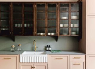 Pale pink painted kitchen cabinets with wooden cupboards above and gray countertops.