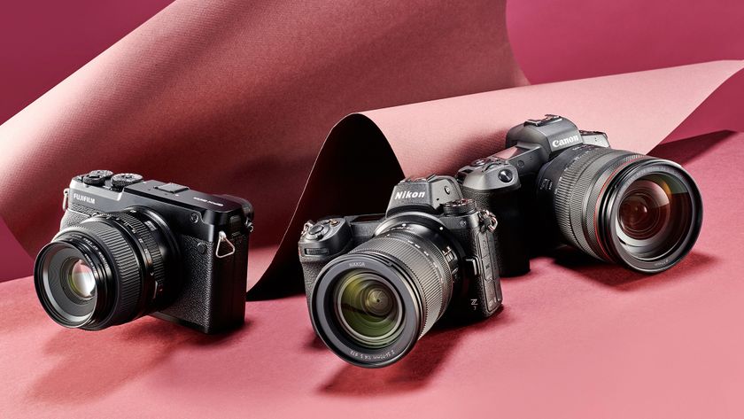 Three digital cameras on a pink paper backdrop: a Fujifilm, Nikon Z7, and Canon, showcasing their distinct designs and lenses