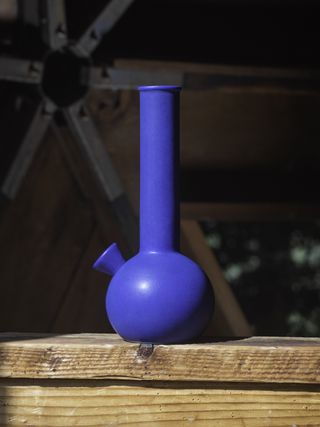 A blue bong with a round base and a long neck on a wooden shelf.